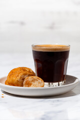 black coffee in a glass and mini croissant, vertical