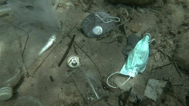 Dead Greater weever fish (Trachinus draco) hitting trapped in plastic bag lies inside plastic bag on the seabed among the medical face mask, plastic and other garbage. Plastic pollution of Ocean.  