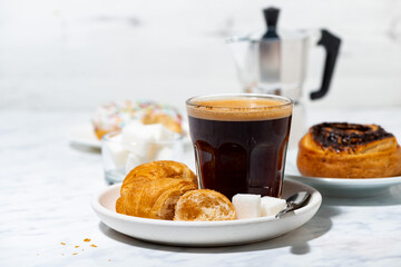 black coffee in a glass, mini croissants and a sweet bun