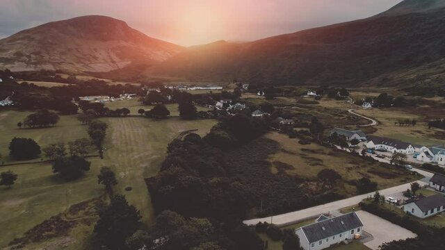 Sunset over mountain at village aerial. Nobody nature landscape at sun set. Cottages, houses at road. Whiskey distillery at valley. Cinematic Loch-Ranza, Arran island, Scotland, United Kingdom, Europe