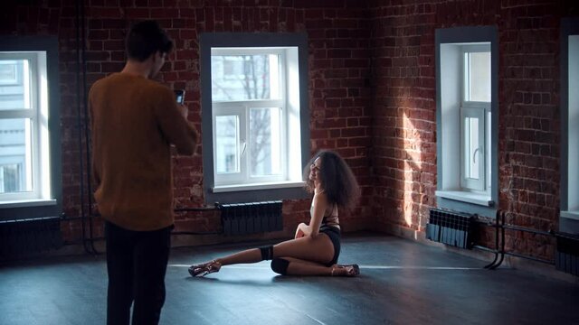 Strip dancing in the studio - young attractive curly woman in tiny outfit sexy dancing on the floor and man taking a photo of her