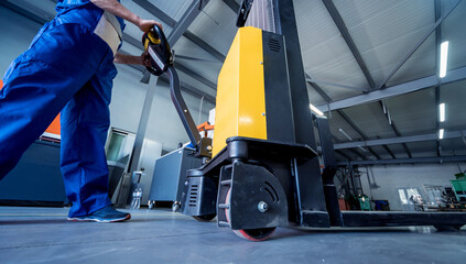 A worker in a warehouse uses a hand pallet stacker to transport pallets.