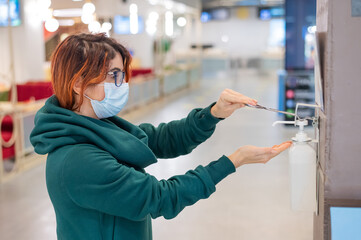 A woman uses a wall sanitizer in a public place. Close-up of female hands treating with antiseptic
