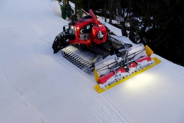 Working red snow groomer on the ski slope in the evening. Dolomites, Italy, Puster Valley/Alta Pusteria, South Tyrol.
