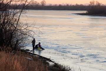 Fototapeta na wymiar Fishermen on an evening winter fishing on the ice of the Staritsa River