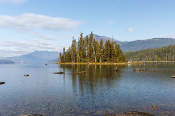 Evergreen forest on Emerald Island in Lake Wenatchee with mountain background and calm water.