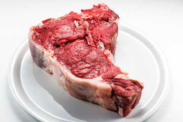 Raw T-bone steak on white round plate