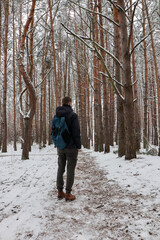 A traveler with a big bag walks through a snowy forest. Man's winter walk. Photo in full growth.