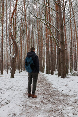 A traveler with a big bag walks through a snowy forest. Man's winter walk. Photo in full growth.