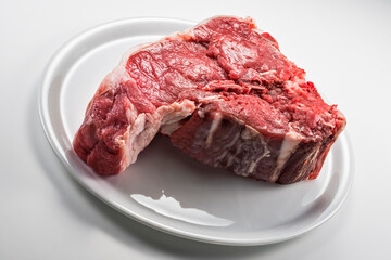 Raw T-bone steak on white round plate