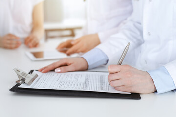 Unknown woman-doctors at work consulting patient. Female physicians filling up medical documents or prescription, close-up