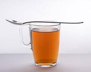 A cup of tea in glass utensil with metal spoon on the cup in minimalistic style
