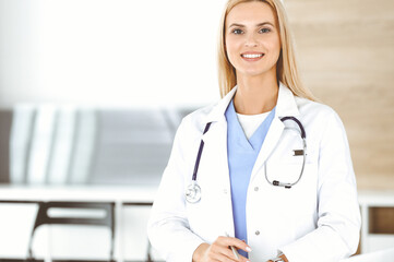 Woman-doctor at work in clinic happy of her profession. Blond female physician controls medication history record and medical exam results. Medicine concept