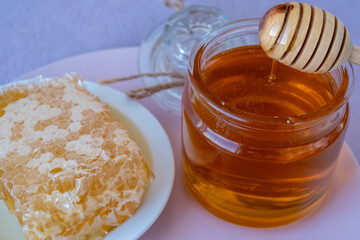 a woman's hand takes honey on a wooden stick from a full jar of honey with honeycombs on a plate