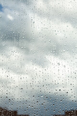 Close up of a window with rain drops falling down. Focus on rain drops. Rain drops on rainy day on outside window glass with blurred edges. Rain outside window pane in spring day.