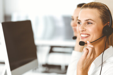 Blond female customer service representative and her colleague are consulting clients online using headset. Call center and business people concept