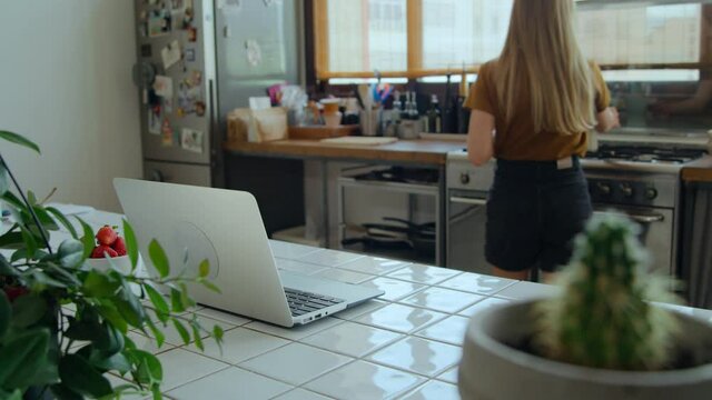 Young woman work from home on laptop on kitchen counter. Make and pour coffee in cup, communicate and chat with coworkers team. Stay in touch, bee effective and productive from home office