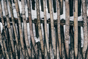 Old wooden village fence made of branches under snow