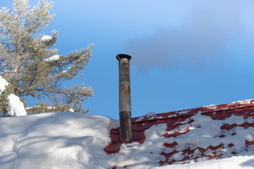 Smoke from the chimney on snow covered roof of house
