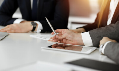 Unknown businessmen and woman sitting, using laptop computer and discussing questions at meeting in sunny office, close-up. Success concept