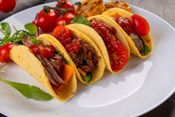traditional Taco with meat, tomatoes, beans, chili peppers and grilled corn on a white plate and dark background for the restaurant menu
