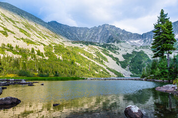 Lake at foot of mountain range. River in mountain valley along rocks. Summer morning in mountains of Siberia