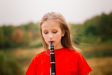 Young attractive girl playing clarinet, ebony in fall park