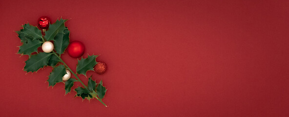 Christmas Composition Concept.  Green ilex brenches with red christmas balls on red background. Flat lay, top view.