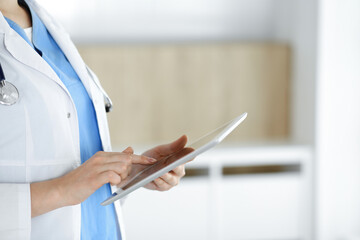 Unknown woman-doctor standing in clinic and using tablet pc, close-up. Data in medicine and healthcare