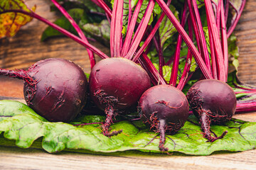 Beetroot tubers with green leaves on wooden table. Preparation of fresh salad. Fresh vegetables for vegetarian cooking. Beets on street market stall.