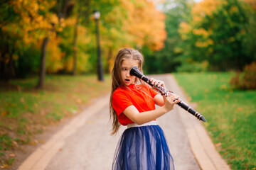 Young attractive girl playing clarinet, ebony in fall park