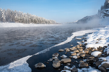 Winter river with frosty fog over water. Snow trees on shore.