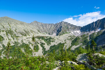 Fototapeta na wymiar Panoramic view of rocky ridge. Mountains on horizon under cloudy sky. Travel through mountain valley on sunny day.