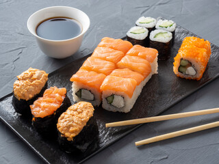 a variety of Japanese rolls and sushi on a textured plate. Side view. bamboo sticks of ginger and...