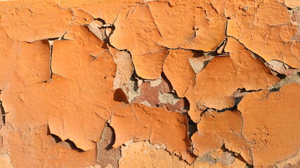 a fragment of an old exterior wall with cracked layers of aged brown paint and deep cracks in its structure, brightly lit by sunlight aging texture of a retro surface