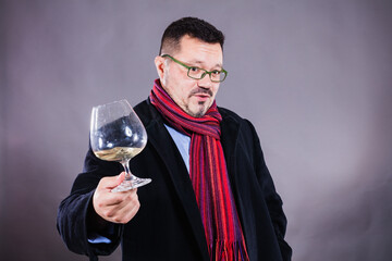 Solid cheerful man in coat and kerchief standing with glass of wine