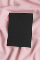 Black invitation card mockup on a soft pink textile. 5x7 ratio, similar to A6, A5.