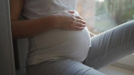 Attractive pregnant woman sitting by window at home. High quality 4k footage - Powered by Adobe