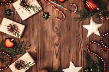 Christmas and New Year rustic traditional background with copy space. Festively decorated cedar branches on a dark brown old wooden board. Gift boxes, balls, stars and cane lollypops. Place for text.
