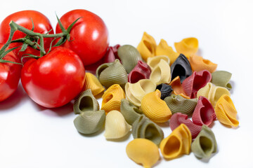 Farbige getrocknete Schneckenpasta mit roten Strauchtomaten vor weissem Hintergrund