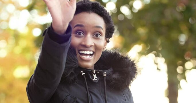 Afro american girl black woman wears outerwear peeps out boyfriend friend looks into distance searching for familiar face waving hand in greeting advice to come up to herself standing alone outdoors