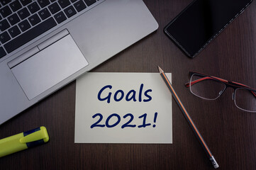 Goals 2021 card. Top view of office table desktop background with laptop, phone, glasses and pencil with card with inscription we can do it.  Business concept.