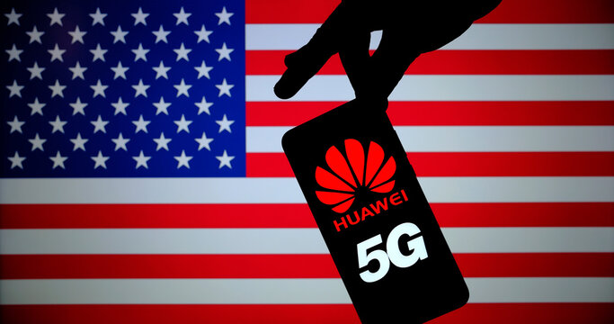 Huawei logo on smartphone silhouette and hand pointing at it. The US blurred flag on the background screen. NOT A MONTAGE, real photo. Stone /UK - July 16 2020: 