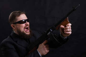 Mature bearded man in sunglasses dressed in suit with tommy gun