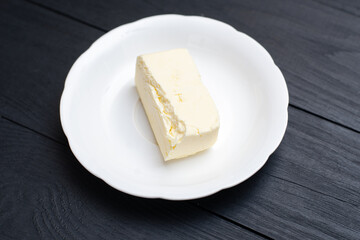 A piece of butter on a plate. On a black wooden background.