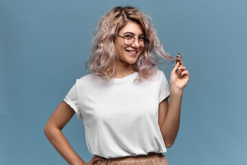 Youth, beauty, style and fashion concept. Portrait of cute playful young woman with pinkish hair and nose ring posing isolated in round glasses, looking at camera with charming flirty smile - obrazy, fototapety, plakaty