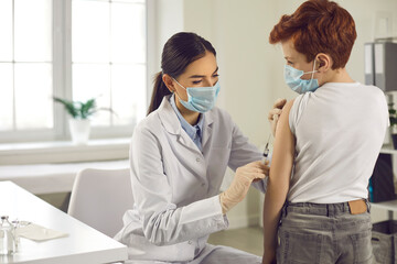 Professional nurse in a medical face mask giving a flu shot to her little patient