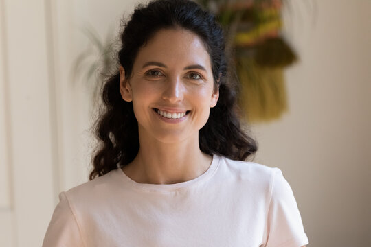 Head shot portrait smiling attractive woman looking at camera, beautiful young female with toothy smile standing at home, posing for profile picture, happy blogger recording vlog, video call