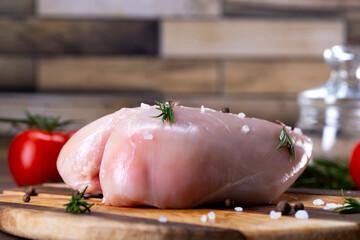 Raw chicken breasts on a cutting board with herbs and tomatoes © Natallia
