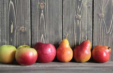 Red apples and pears stand on a wooden surface.